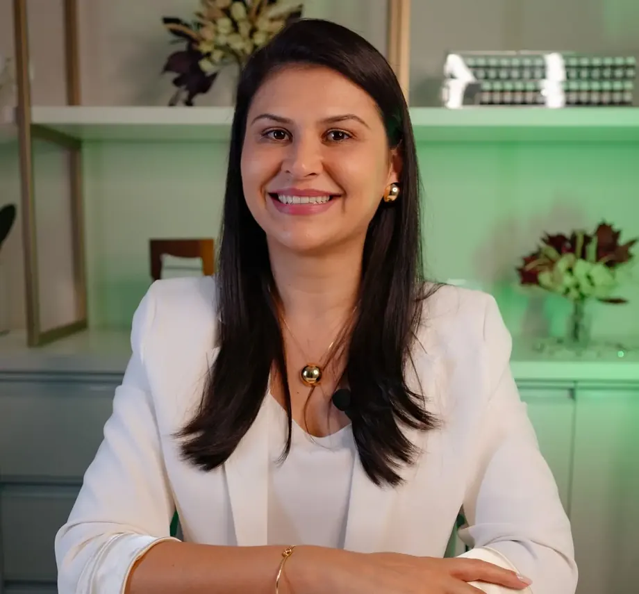 Dra. Elisangela de Andrade, sorrindo, de blazer branco, na clínica